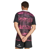 Wearing the adidas All Blacks 26/27 Training Jersey – South Africa Tour, which features a striking purple and black pattern, along with black shorts, a person stands hands behind their back and facing away, perhaps getting ready for the upcoming tour in South Africa.