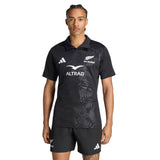A person wearing the adidas All Blacks Greatest Rivalry Performance Home Jersey stands facing forward against a plain white background, paired with black shorts.