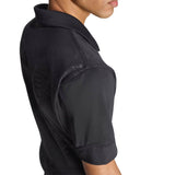 A person shown from the side, with their face partially visible, is wearing the All Blacks Greatest Rivalry Performance Home Jersey by adidas—a black short-sleeve collared shirt inspired by performance rugby designs.
