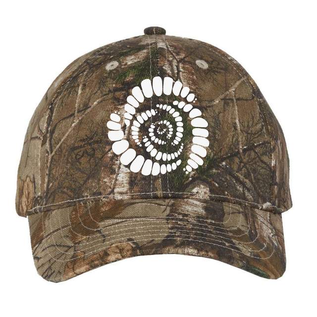 The Missoula All-Maggots Realtree Camo Cap by EMB S&S Activewear features a distinctive white spiral pattern on the front that resembles teeth or a fossil. This adjustable cap blends unique design with classic outdoor style.