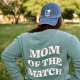 Woman in a park wearing a green sweatshirt reading "Rugby Mom Pride" and an I Heart Rugby Moms Cap by Modish Rugger.