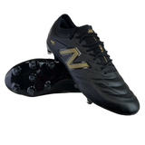 The New Balance 442 v2 Elite FG Wide Boots in Black/Metallic Gold feature a pair with one upright and the other on its side to display the studded sole, perfect for those needing wide boots for firm ground.