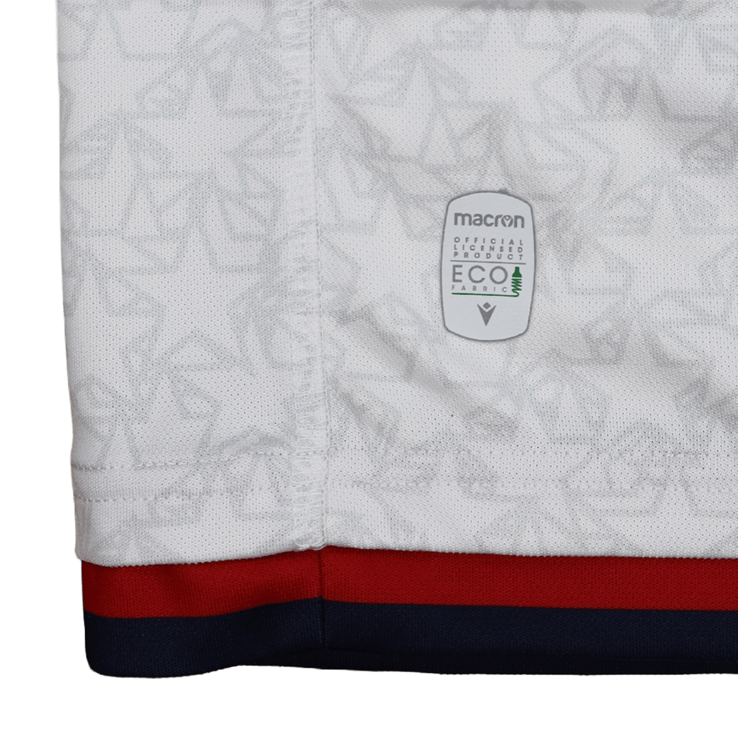 Close-up of the bottom edge of the Old Glory DC MLR 25/26 Replica Away Jersey by Macron, featuring a subtle geometric pattern, red and blue trim at the hem, and a Macron Eco label.