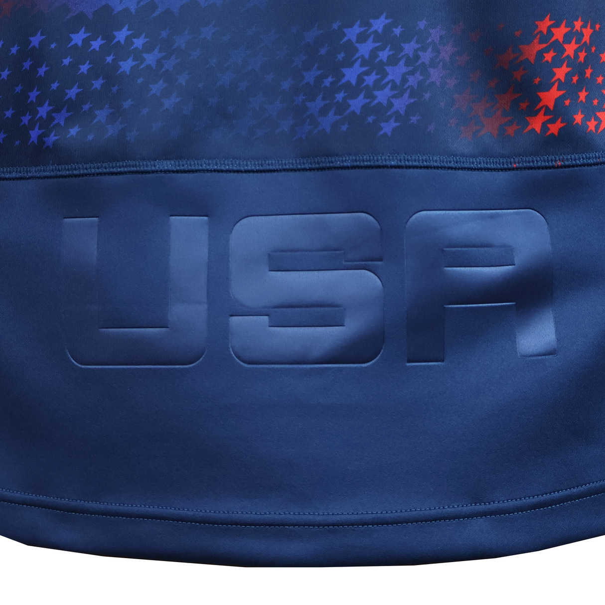 A close-up of the USA Rugby 25/26 Away Replica Jersey by Macron, featuring "USA" in bold raised letters and a red and blue star pattern above.