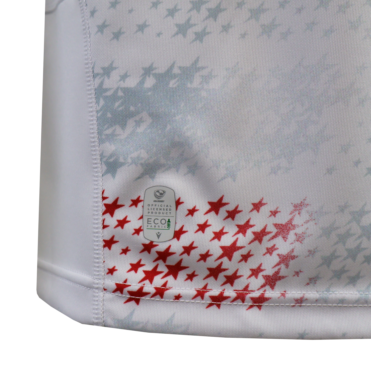 Close-up of white fabric with red and gray stars and an "Eco" tag near the hem, from the USA Rugby 25/26 Home Replica Jersey by Macron.