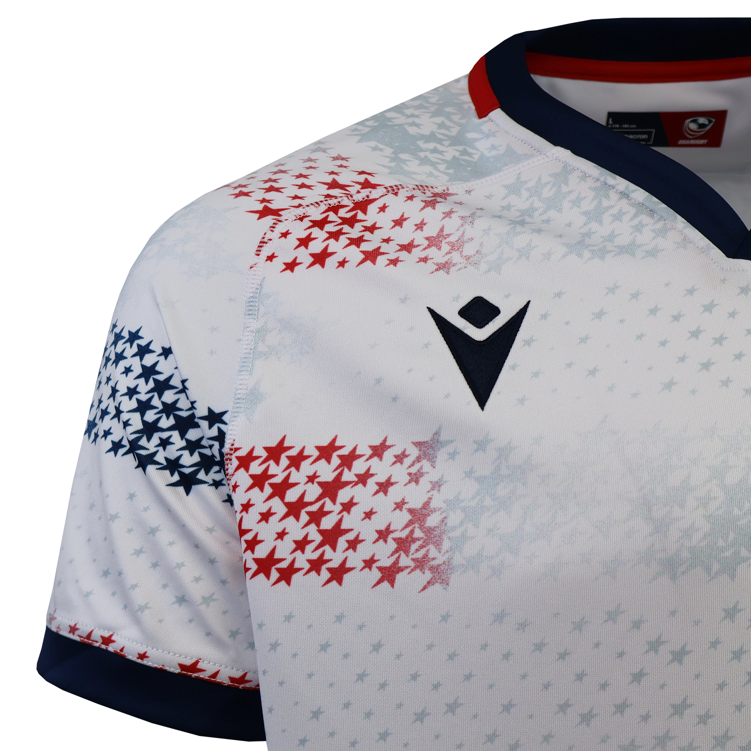 The USA Rugby 25/26 Home Replica Jersey by Macron features a white base with red and blue star patterns, a navy collar, and a black Macron logo—ideal for USA Rugby fans.