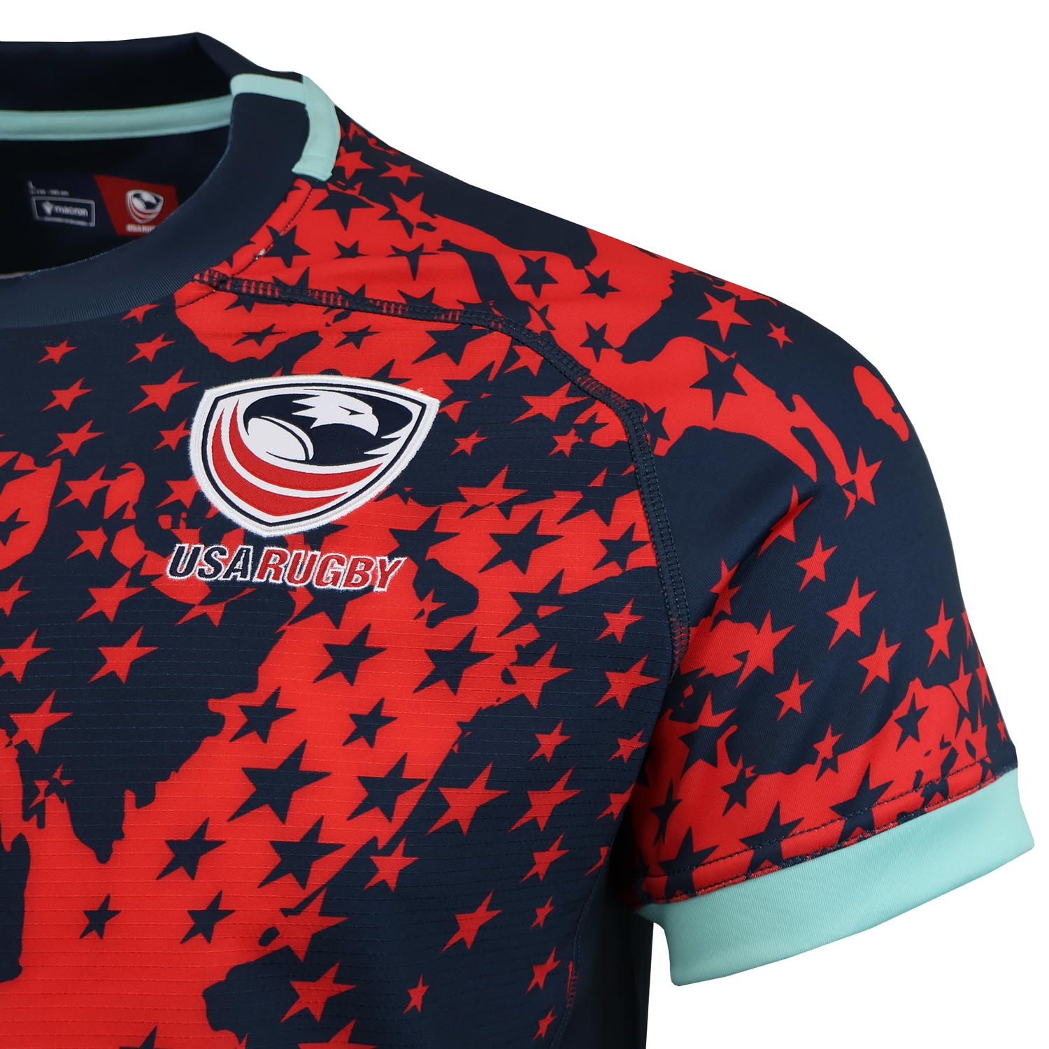 A close-up of the USA Rugby 25/26 Training Rugby Jersey #1 by Macron, featuring a red and navy star pattern, the USA Rugby eagle logo, and light blue trim on the collar and sleeve.