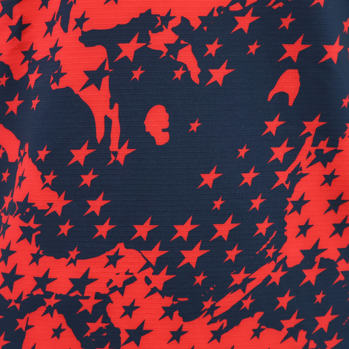 Close-up of the USA Rugby 25/26 Training Rugby Jersey #1 by Macron shows textured horizontal lines with red stars scattered on a dark blue background.