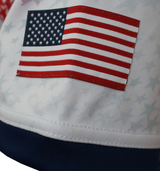 A close-up of a fabric patch showing the United States flag sewn onto white material with faint stars and a navy blue edge, similar to details on the Women's USA Rugby M25/26 Home Replica Jersey by Macron.