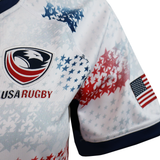 Close-up of the Women's USA Rugby M25/26 Home Replica Jersey by Macron, featuring a stylized eagle logo, red and blue star patterns, and an American flag patch on the sleeve—ideal for fans wanting an authentic Macron jersey.
