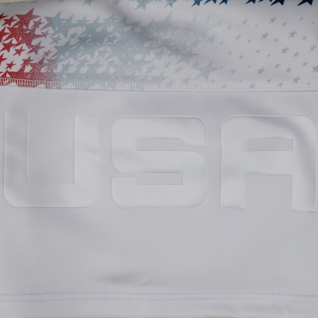 Close-up of the Women's USA Rugby M25/26 Home Replica Jersey by Macron, featuring "USA" in raised letters and a background of red, white, and blue stars.