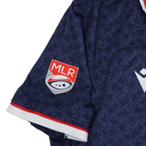 Close-up of the Old Glory DC MLR 25/26 Replica Home Jersey by Macron shows a navy sleeve with the MLR logo patch, red and white trim, and a subtle geometric pattern.