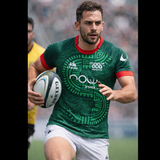 A rugby player wearing the Las Serpientes Mexico Rugby Replica Jersey by Credo Rugby runs with the ball during a match, with another player and a referee seen in the background.