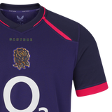 Close-up of the England 26/27 Replica Alternate Jersey by Castore: a navy blue shirt with pink accents, featuring a white “O2” logo and an embroidered gold rose emblem on the chest—a striking replica from Castore’s Rhodonite alternate kit.