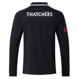 The Bath 26/27 Classic Long Sleeve Home Jersey by Castore is a black long-sleeve shirt, shown from the back. “THATCHERS” appears in white lettering across the upper back, and a red patch accents the right sleeve, giving it a heritage rugby shirt vibe.
