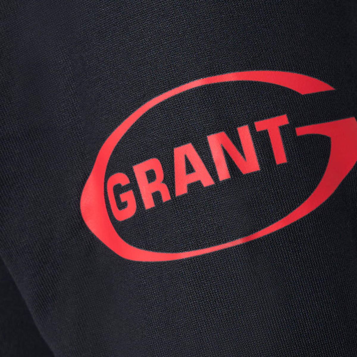 Close-up of black fabric from the Bath 26/27 Classic Long Sleeve Home Jersey by Castore, featuring the word “GRANT” in red, partially enclosed in a red oval outline—evoking classic heritage rugby shirt details typically seen in Castore long sleeve designs.