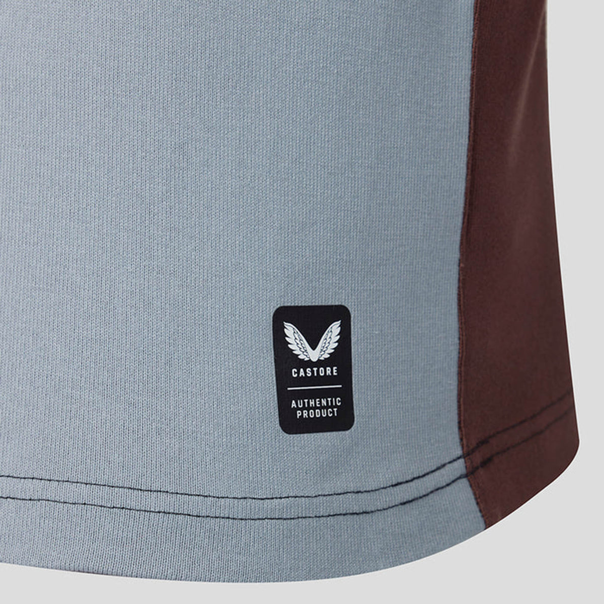 Close-up of the bottom hem of the Harlequins 26/27 Classic Long Sleeve Home Jersey by Castore, showcasing grey fabric with a black Castore “Authentic Product” label and visible stitching—a signature detail that highlights the quality craftsmanship of this classic home jersey.