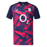 The England 26/27 Pre-Match Top by Castore is a short-sleeved shirt with a navy and bright pink geometric pattern, featuring the O2 logo and a white rose emblem on the chest.