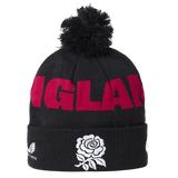 The England 26/27 Bobble Beanie by Castore is a black knit beanie featuring a pom-pom, bold red “ENGLAND” lettering, and a white rose emblem on the fold—an essential winter accessory for England supporters and the perfect Castore beanie for chilly rugby match days.