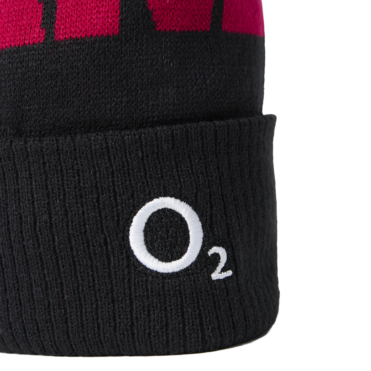 A close-up of the England 26/27 Bobble Beanie by Castore, featuring a black knit body with a red upper section and a white “O₂” logo embroidered on the folded cuff—this classic Castore beanie is the perfect winter accessory for any England rugby supporter.