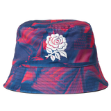 The Castore England 26/27 Reversible Bucket Cap features blue and red patterns and a white embroidered rose on the front, taking inspiration from the iconic England rugby cap.