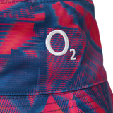 Close-up of a fabric featuring a red and blue geometric pattern with a white “O₂” logo embroidered on it—this detail highlights the premium finish of the Castore England 26/27 Reversible Bucket Cap, designed for lightweight sun protection with modern style.