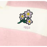 The EMB Augusta Women's Vintage Japan Prep Street Rugby Crop features three pale pink flowers with yellow centers and green stems above "1932," set on pink and white striped fabric for a retro rugby style.