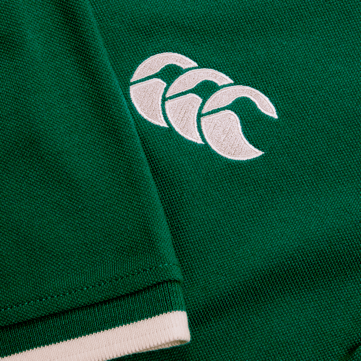 Close-up of a green fabric with a white embroidered logo featuring three overlapping shapes, reminiscent of the craftsmanship on an Ireland 24 Team Polo by Canterbury, complete with ribbed collar and cuffs.