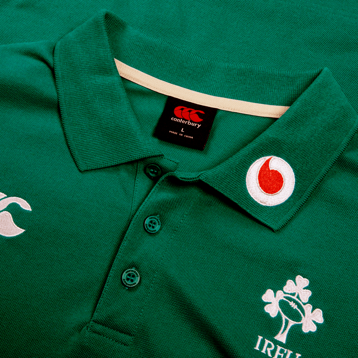 The Ireland 24 Team Polo by Canterbury is a green rugby jersey featuring ribbed collar, cuffs, three buttons, and embroidered logos of Canterbury, Vodafone, and a shamrock with "IRELAND.