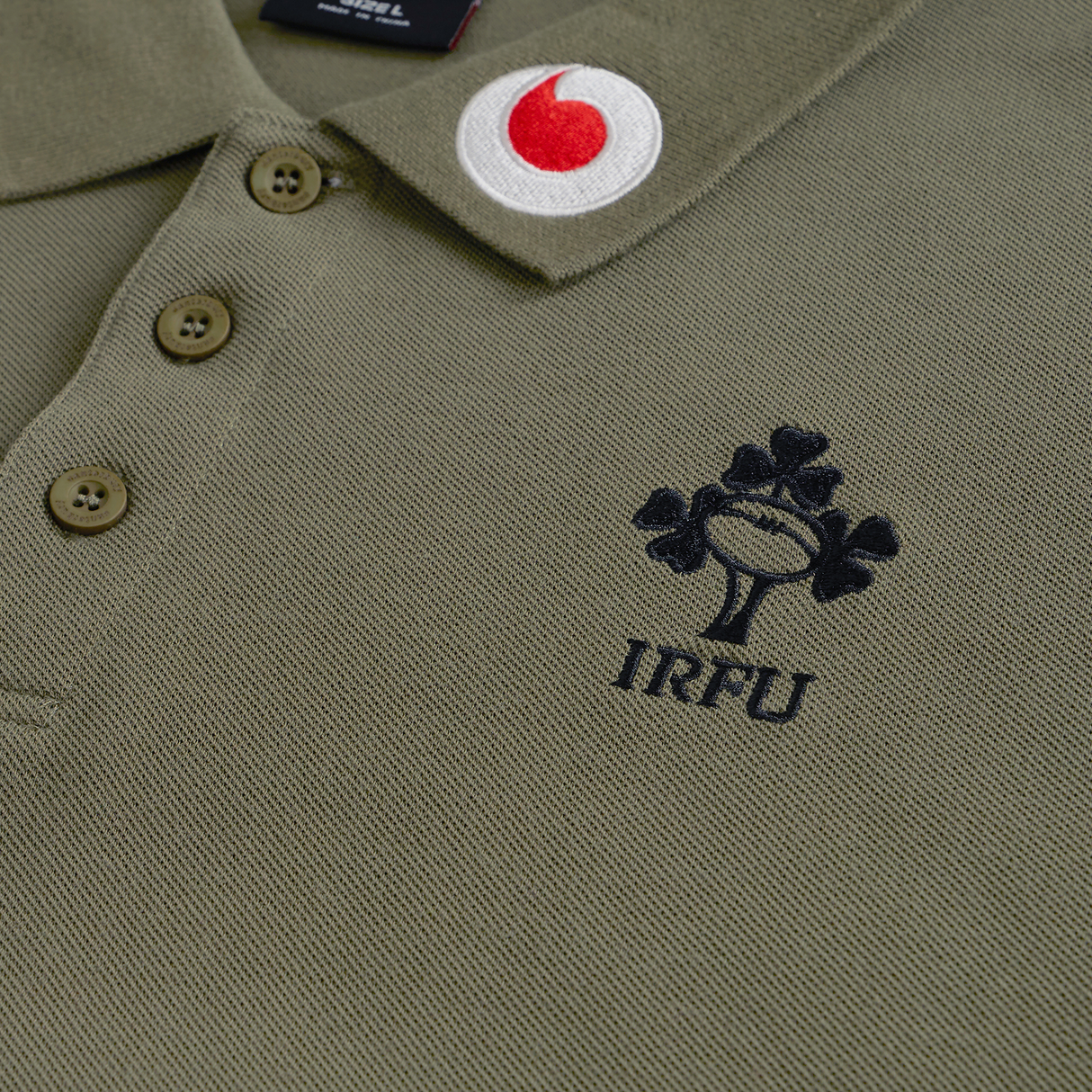 Close-up of the Ireland 25/26 Team Polo by Canterbury, a green polo shirt with the IRFU logo and a red-and-white circular patch on the collar.