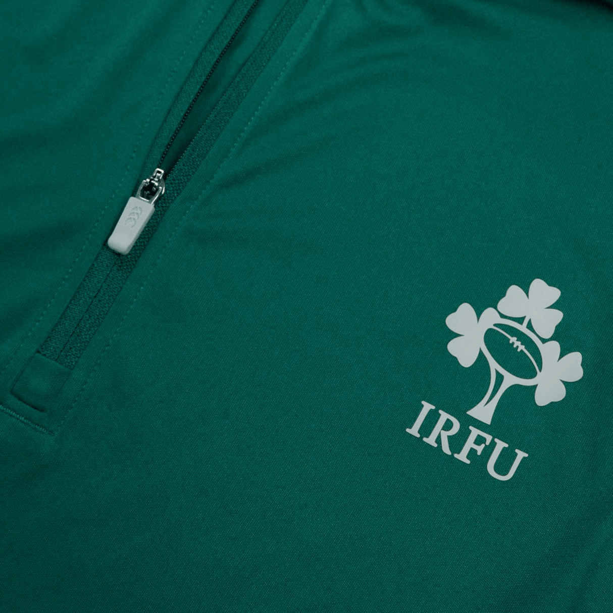 Close-up of the Ireland 24 Vapodri First Layer by Canterbury, showcasing a green garment adorned with the "IRFU" logo, including a rugby ball and shamrocks. This piece incorporates VapoDri technology and features a handy zippered pocket for added convenience.