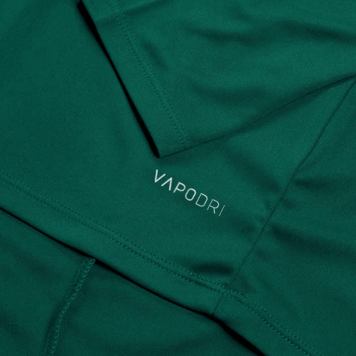 Close-up of green fabric featuring the word "VAPODRI" printed in small white letters. The image showcases the texture and stitching of the Ireland 24 Vapodri First Layer by Canterbury, highlighting Vapodri technology.