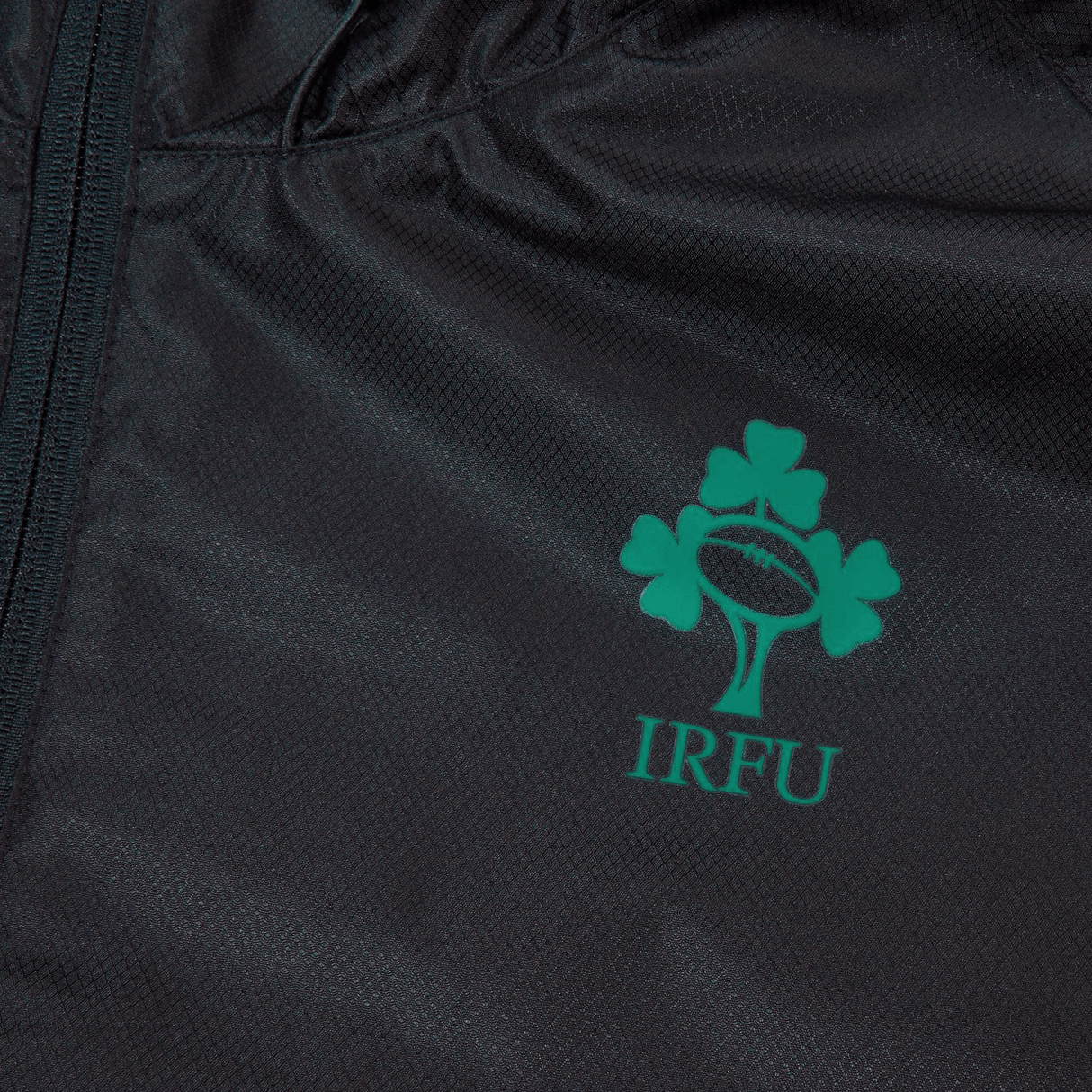 Close-up of a black fabric Ireland 24 Wind Resistant Jacket by Canterbury, showcasing the Irish Rugby Football Union logo adorned with a three-leaf clover and the letters "IRFU" in green. The jacket is equipped with Vaposhield technology for enhanced comfort.