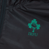 Close-up of a black fabric Ireland 24 Wind Resistant Jacket by Canterbury, showcasing the Irish Rugby Football Union logo adorned with a three-leaf clover and the letters "IRFU" in green. The jacket is equipped with Vaposhield technology for enhanced comfort.