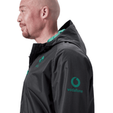 A man in profile view wearing a black Ireland 24 Wind Resistant Jacket by Canterbury, featuring Vodafone branding, Vaposhield technology, and a green hood lining.