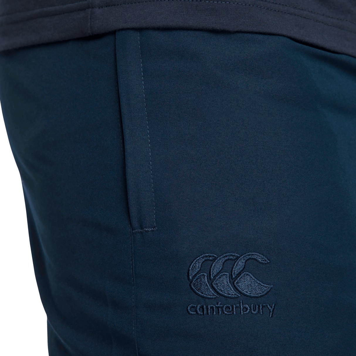 Close-up of dark blue Canterbury Team Tonal Taper Leg Cuffed Trackpant, featuring an embroidered logo on the thigh and a sleek tapered fit.