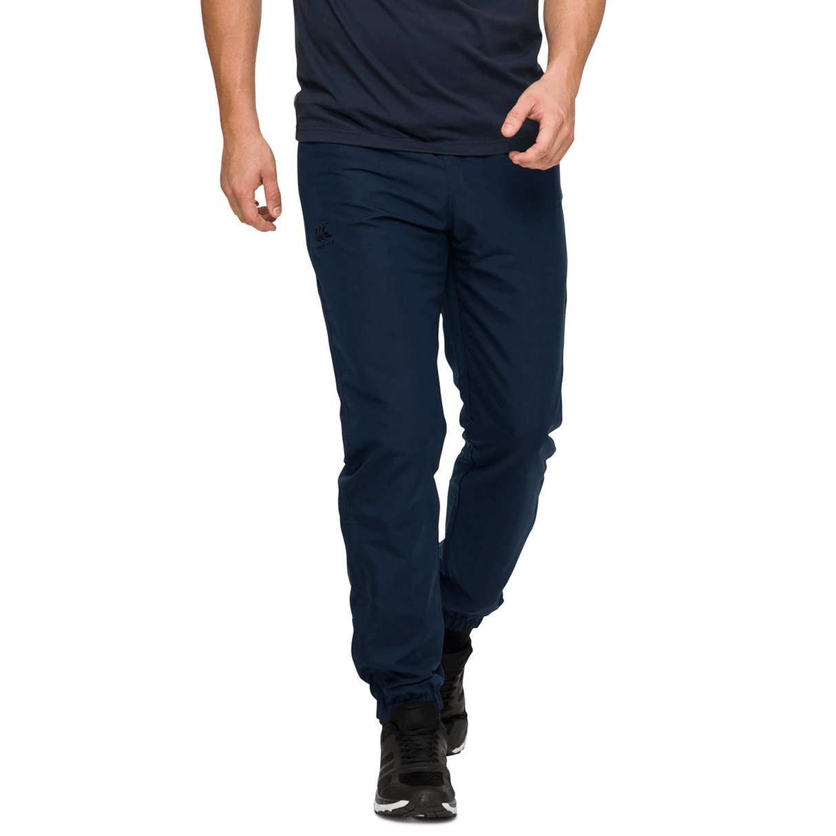 A person energetically walking forward, hands relaxed at their sides, wearing a navy blue T-shirt and Canterbury Team Tonal Taper Leg Cuffed Trackpant.