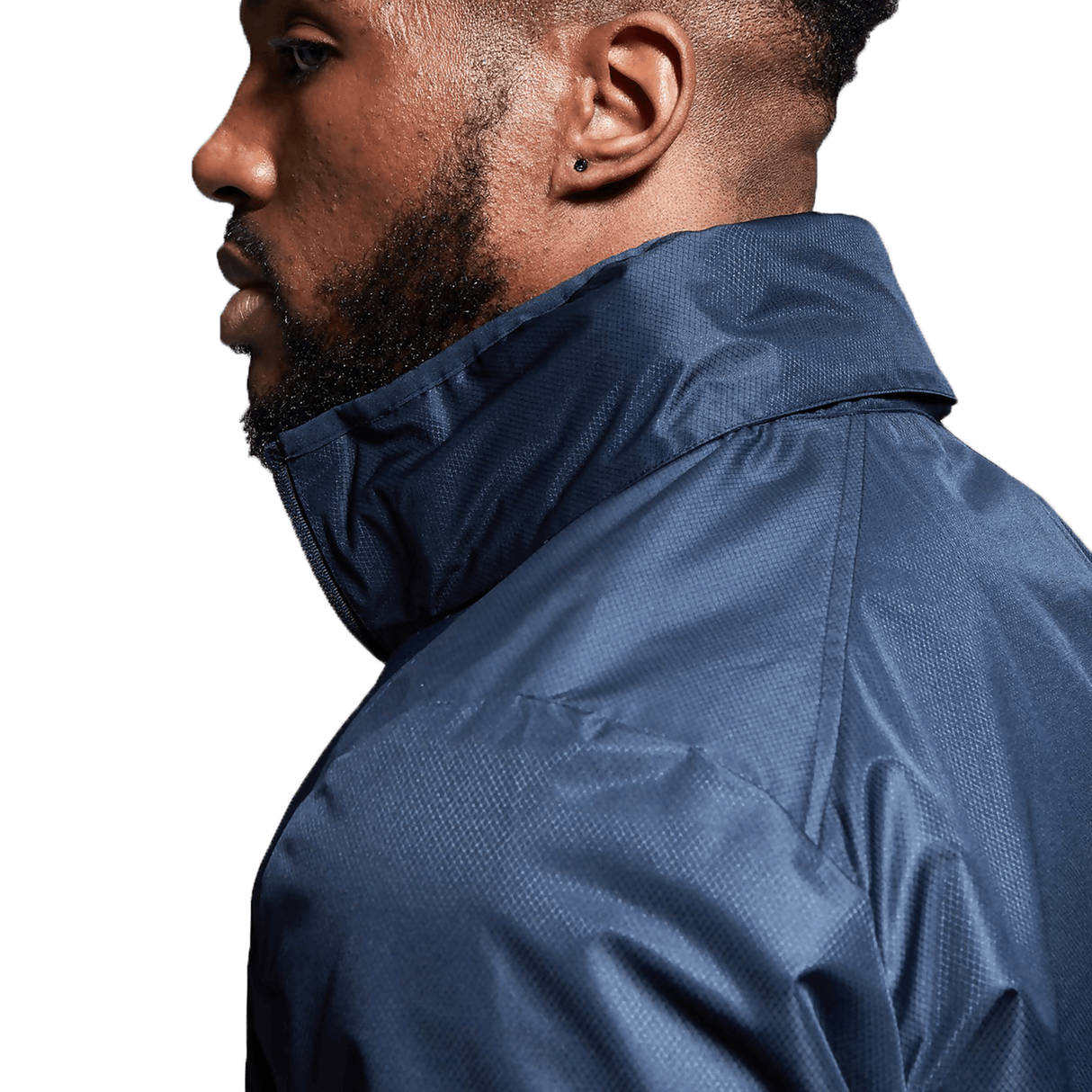 Side profile of a man with a beard wearing a Canterbury Club Vaposhield Full Zip Rain Jacket in navy blue with the collar turned up, featuring VapoShield Technology for water resistance.