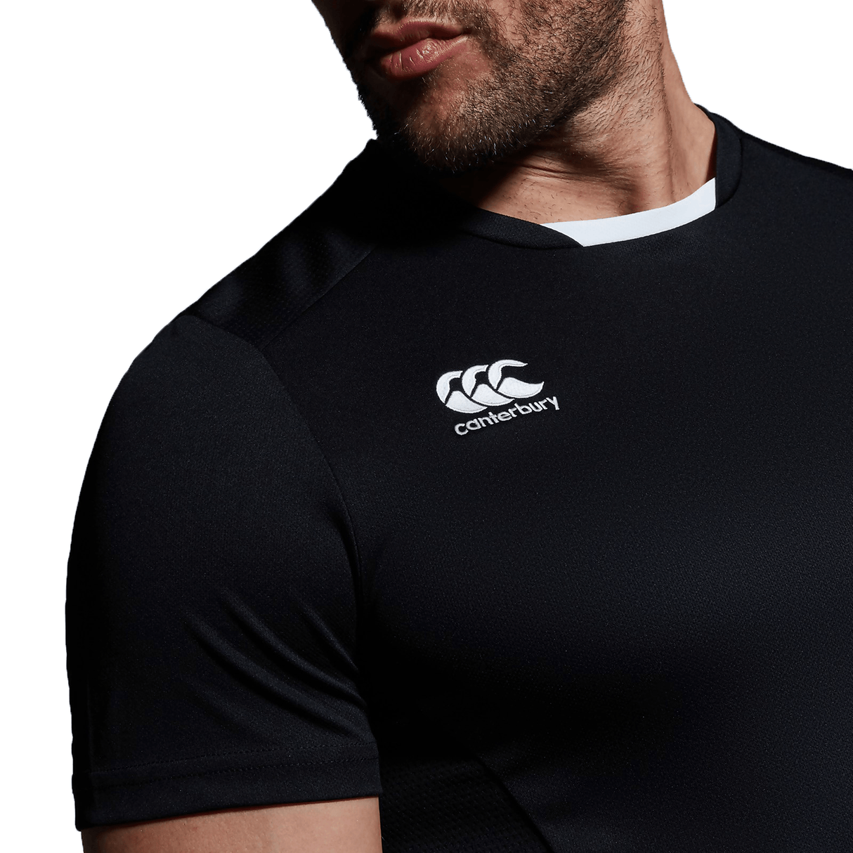 A man wearing a black Canterbury Club Dry Tee with a white Canterbury logo on it.