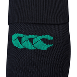 A close-up view of the Ireland 24 Alternate Sock by Canterbury showcases its black knitted fabric adorned with a green logo consisting of three stylized overlapping letters. The sock includes ankle and arch support and features fast-drying performance yarn.