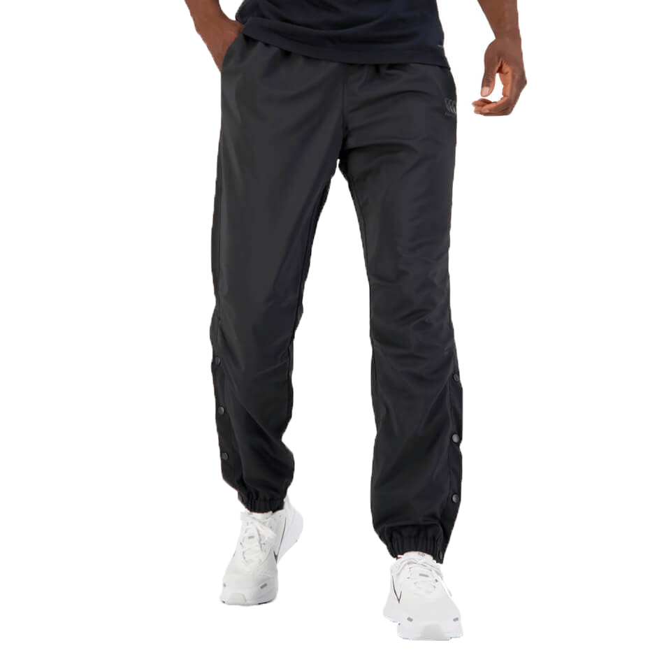 A man stands wearing dark Canterbury Tempo Vaposhield Dome Pant and white sneakers, focusing on the visible details and design of the pants.