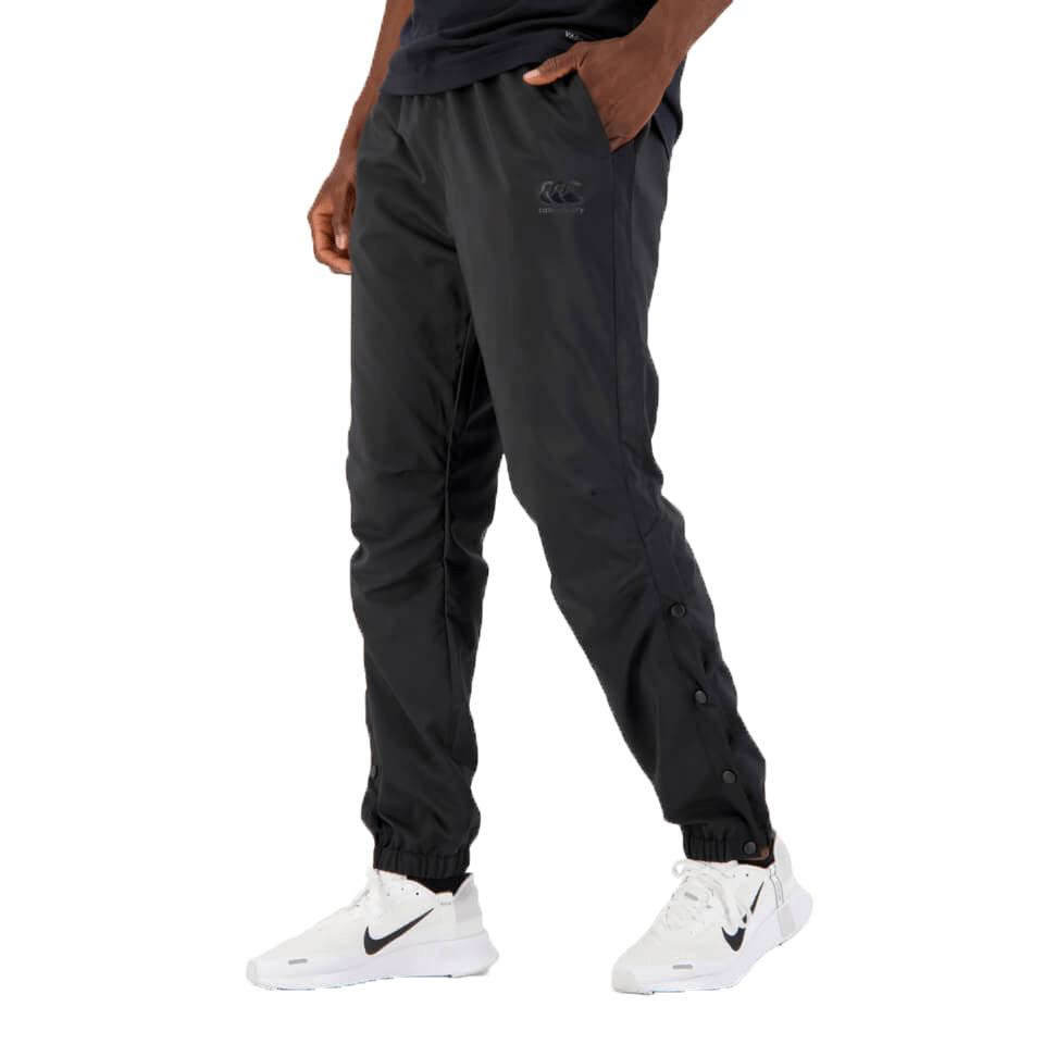 A person wearing black Canterbury Tempo Vaposhield Dome Pant and white sneakers, standing sideways with focus on the clothing.