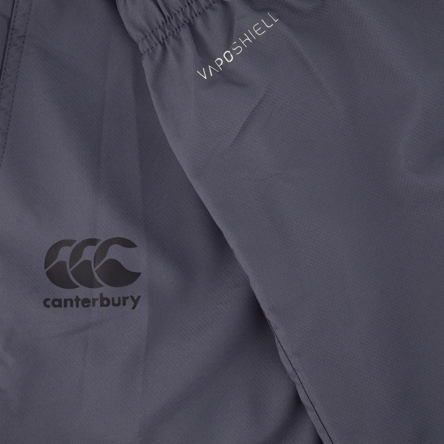 Close-up of the dark gray fabric from the Canterbury Tempo Vaposhield Dome Pant. It features "CCC canterbury" and "VAPOSHIELD" logos with an elastic waistband for comfort and a perfect fit.