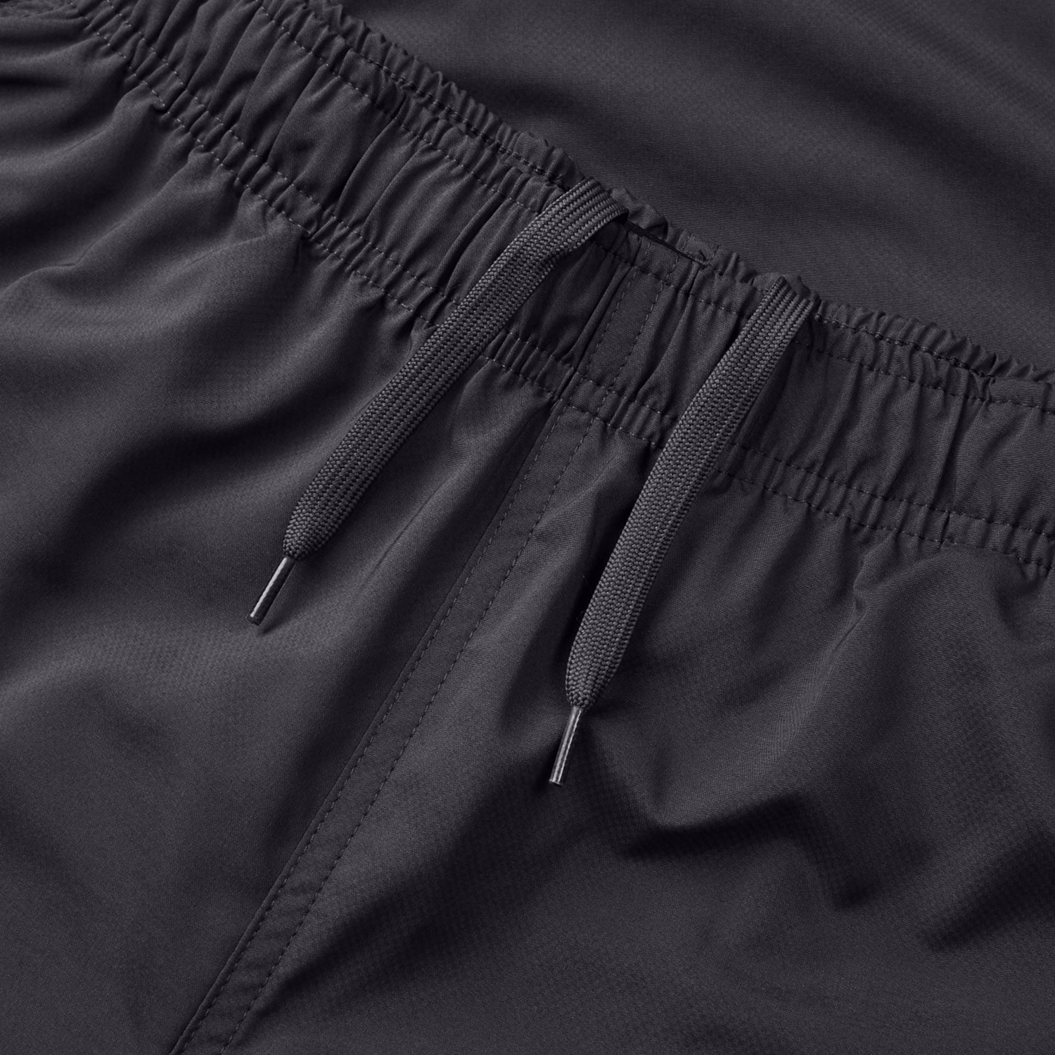 The Canterbury Tempo Vaposhield Dome Pant, a close-up of black athletic shorts, showcases an elastic waistband and adjustable drawstrings. The smooth, breathable fabric offers track pant-like comfort, making it perfect for active wear.