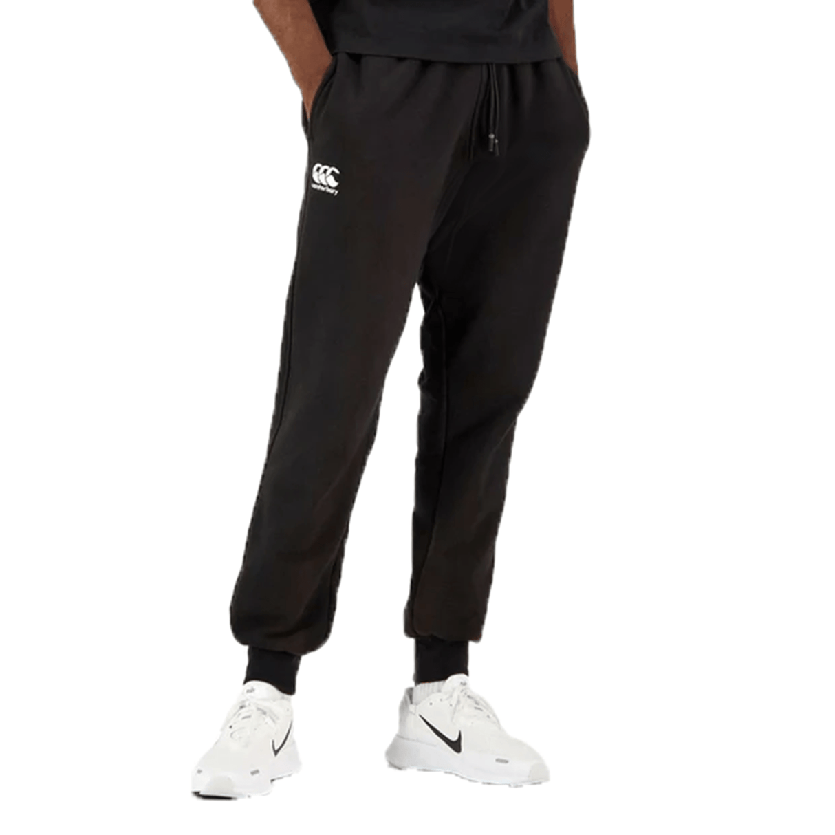 A man wearing black tapered Canterbury Anchor fleece pants with the CCC logo on the left thigh paired with white Nike sneakers, depicted from the waist down.