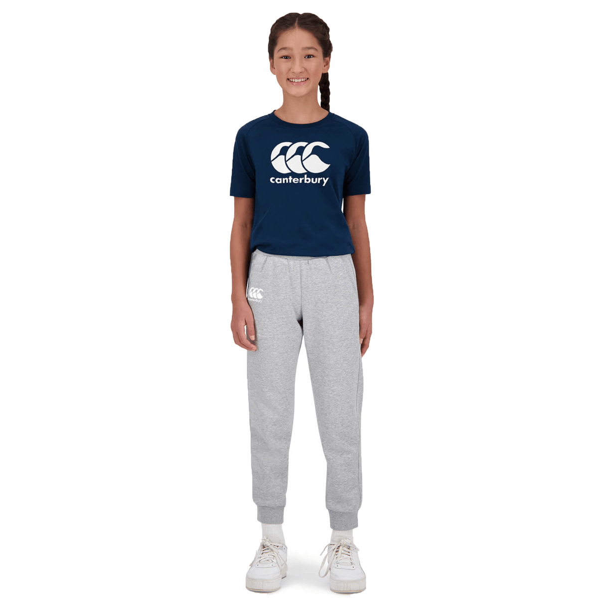 A young girl in navy Canterbury Anchor Fleece Pant t-shirt and gray sweatpants with side pockets, smiling and standing straight against a white background.