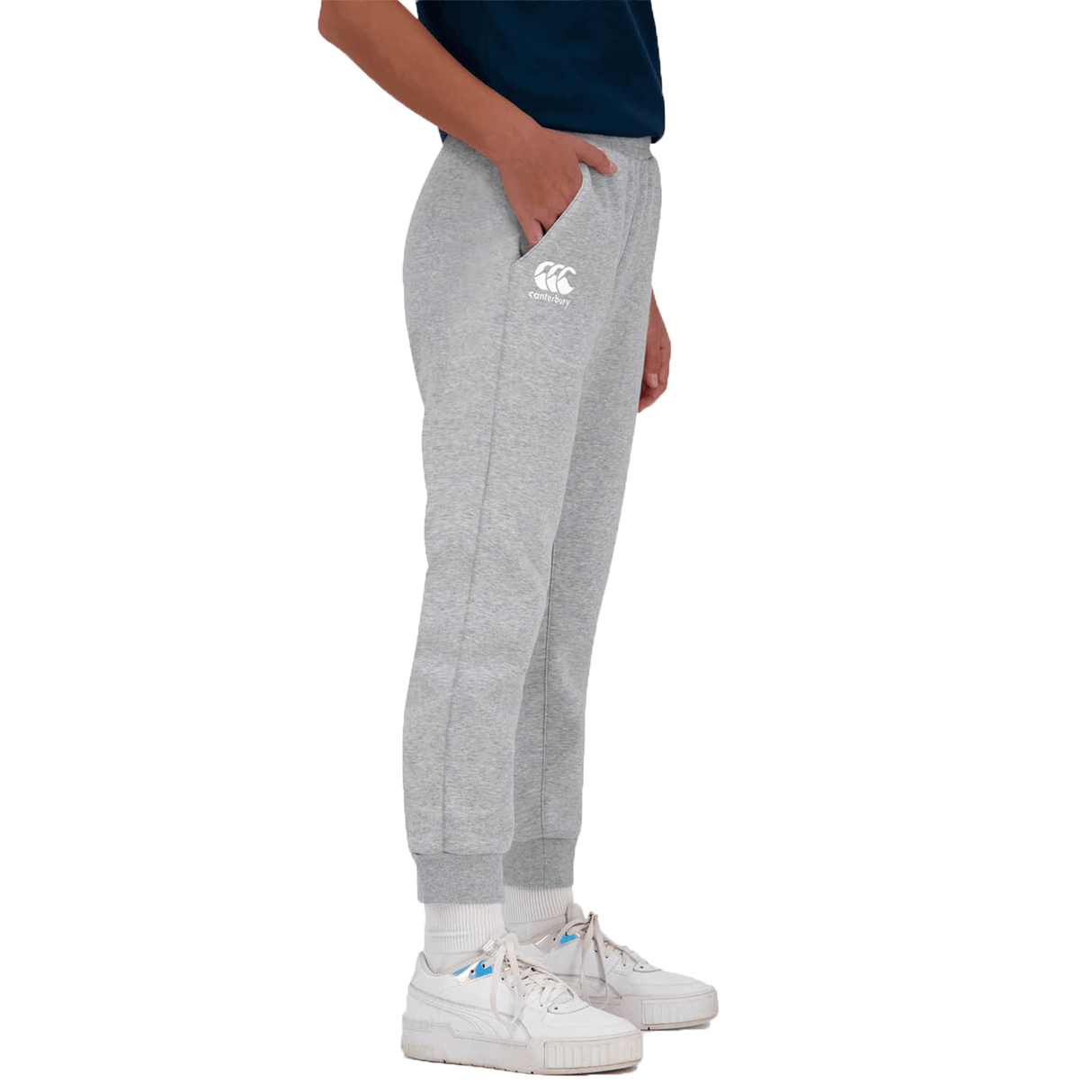 A person standing side-on wearing Canterbury Anchor Fleece Pants with a logo on the left thigh, white socks, and white sneakers.