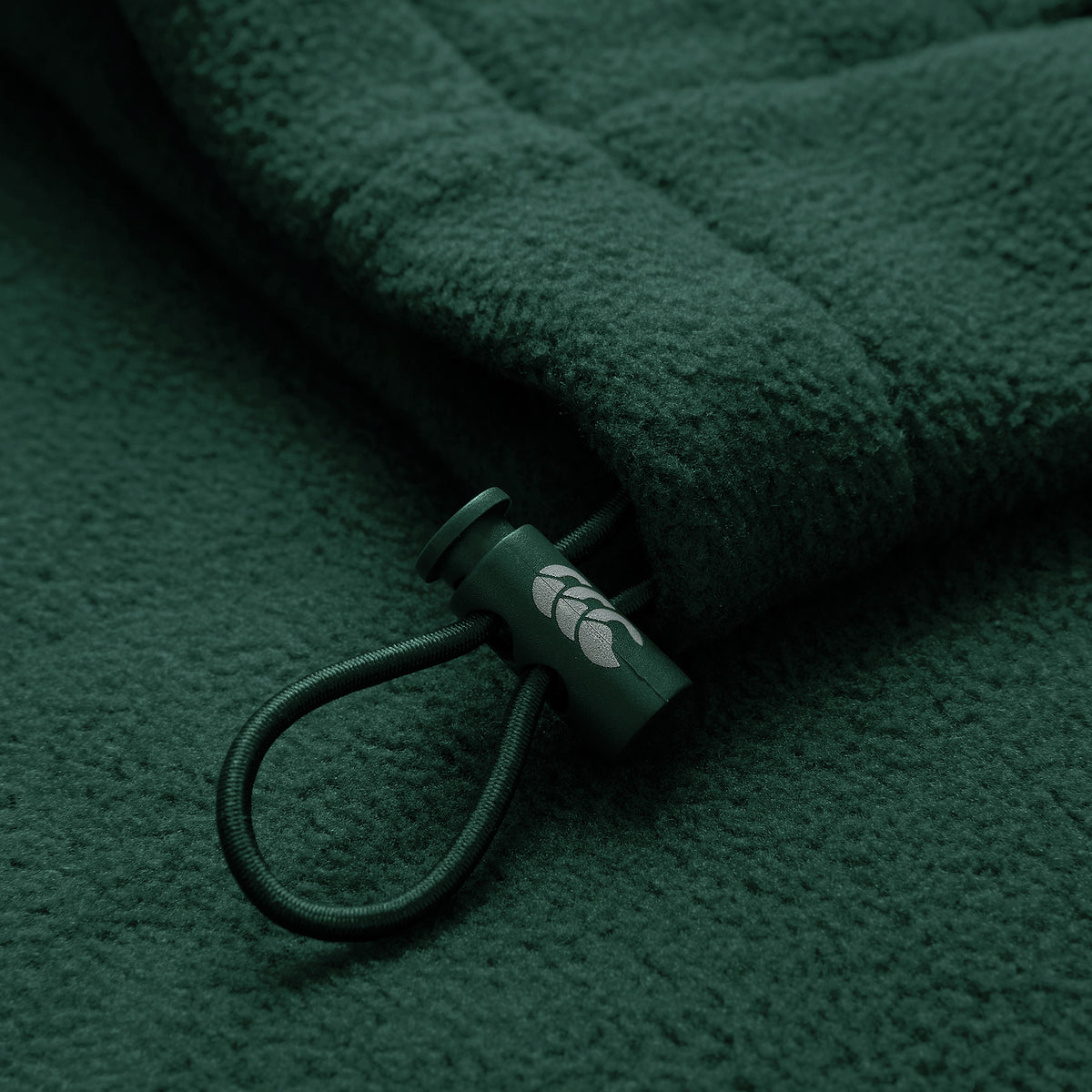 Close-up of the Ireland 26 Retro Fleece 1/4 Zip by Canterbury, showcasing its dark green fleece fabric, cord with a plastic toggle adorned with a small white leaf design—evoking the classic style of vintage Canterbury training pullovers.