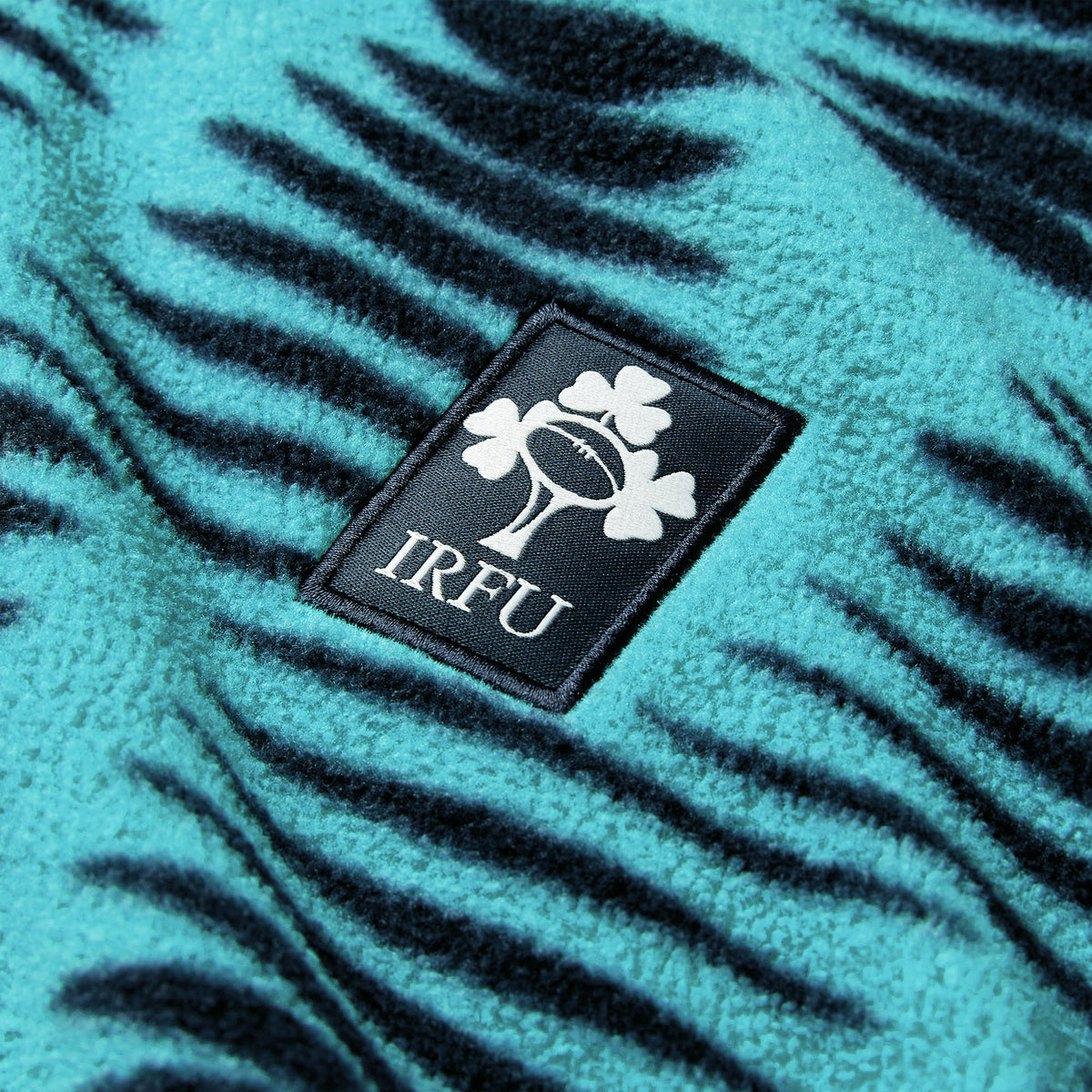 Close-up of the Canterbury Ireland 26 Retro Fleece 1/4 Zip, showcasing its teal and black tiger-striped design and IRFU patch featuring a rugby ball and shamrock.