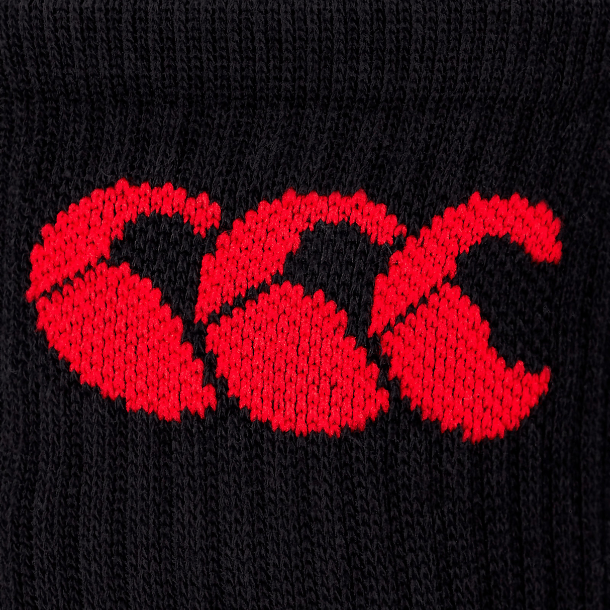 Close-up of a red embroidered Canterbury logo on a black cotton rich fabric.